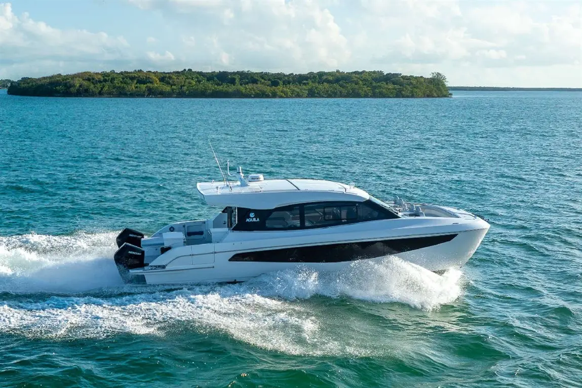 White motorboat cruising on turquoise water with a lush green island in the background under a bright blue sky.